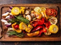 Grilled vegetables on cutting board on dark wooden background