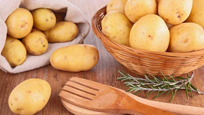 Potatoes in a wooden bowl with a sprig od rosemary and wooden utensils Potatoes in a wooden bowl with a sprig od rosemary and wooden utensils