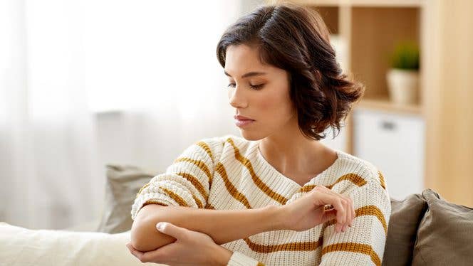 young woman holds and looks at elbow as though in pain young woman holds and looks at elbow as though in pain
